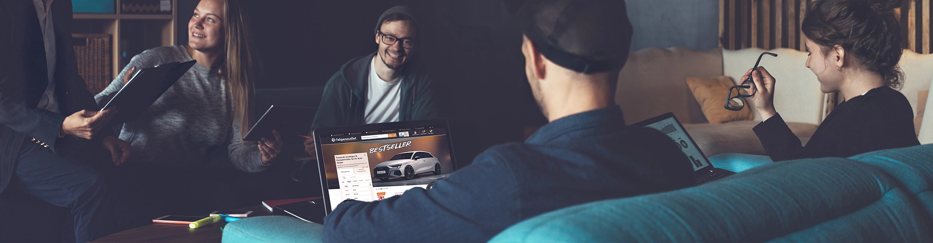 Employees discussing ideas while the Felgenoutlet website is displayed on a laptop.